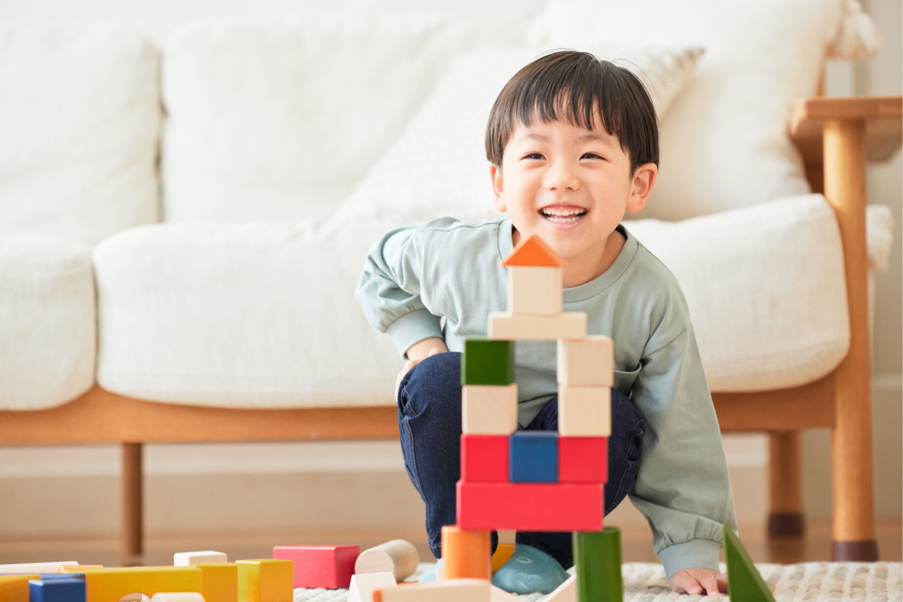 A child smiling while stacking colourful blocks in a cosy home setting.