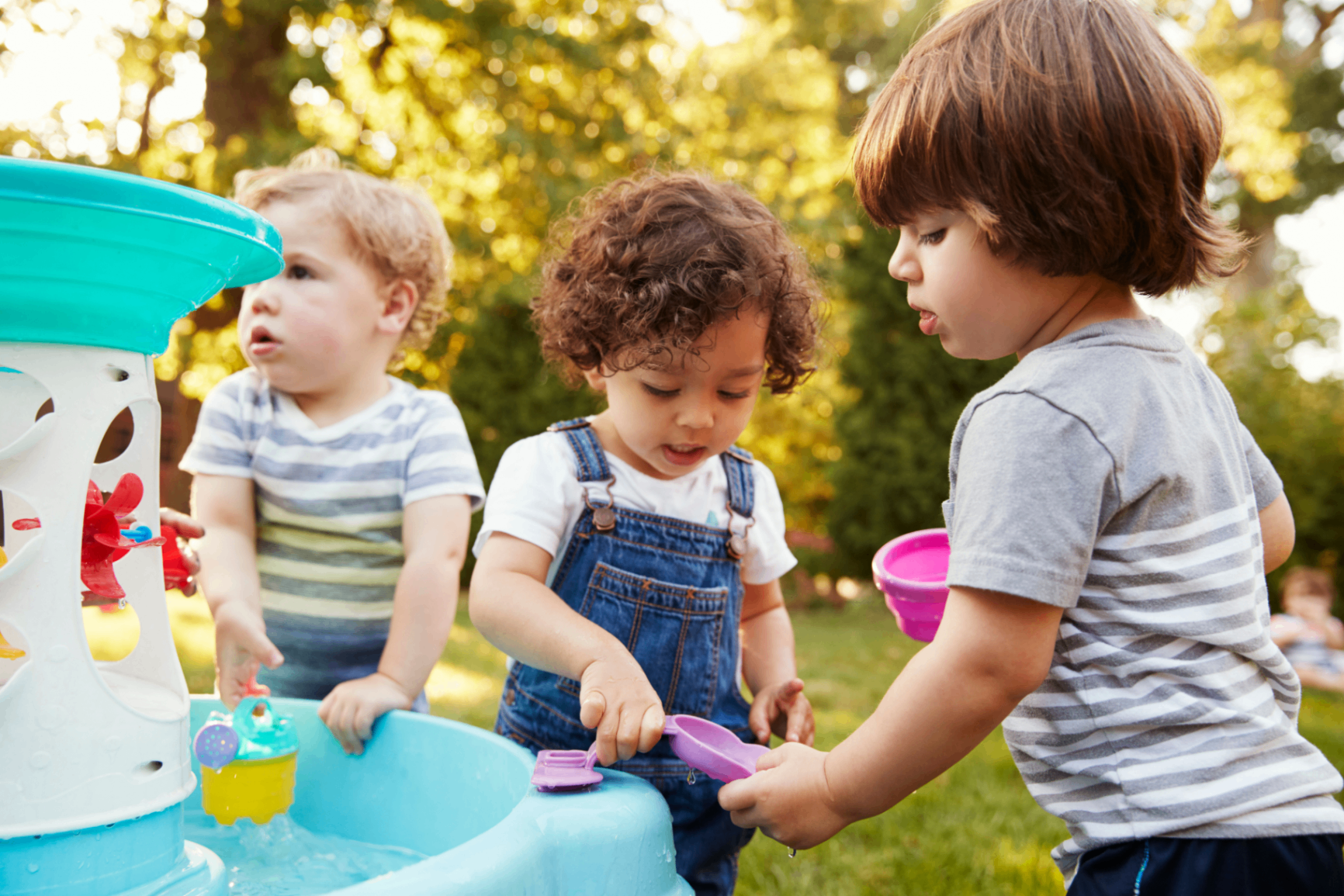 Young children playing together outdoors with water toys in the sunshine.