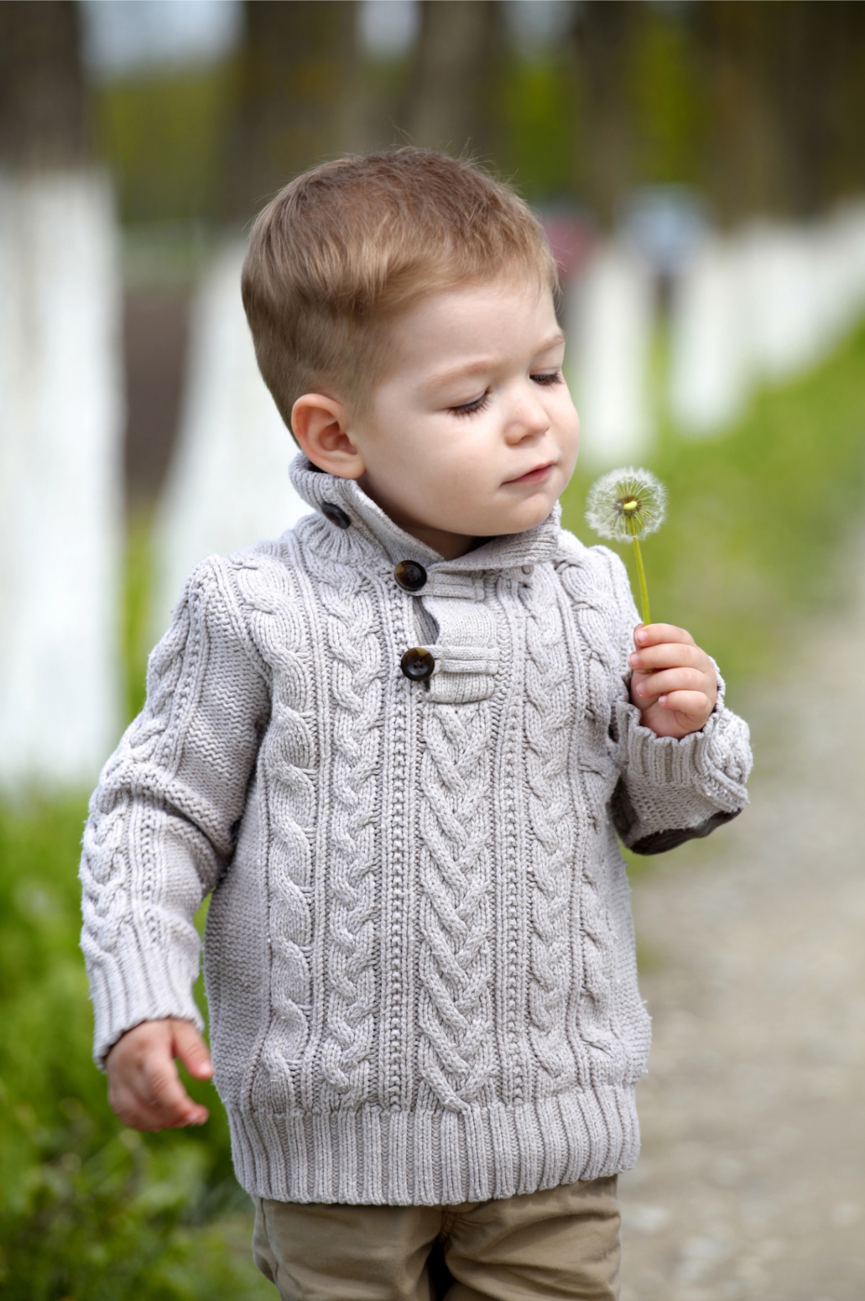 A young child calmly holding a dandelion outdoors.